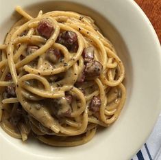 a white bowl filled with pasta covered in mushrooms and sauce on top of a wooden table