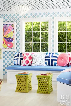 a blue and white living room with colorful pillows on the couch, window seat, and side table