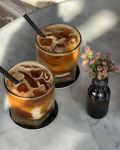 two glasses filled with liquid sitting on top of a table next to a flower vase