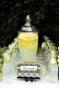 a table topped with lots of glasses and bottles filled with lemonade next to a sign that says lemonade