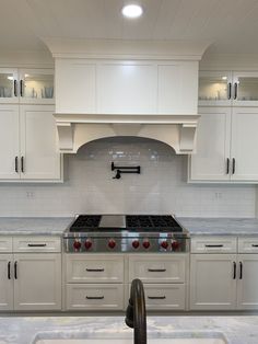 a kitchen with white cabinets and stainless steel stove top oven in the center, surrounded by marble counter tops