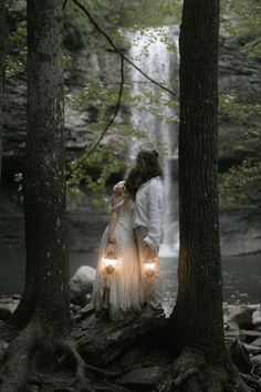 a man and woman standing in front of a waterfall with two lights on their hands