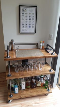 a wooden shelf filled with glasses and bottles on top of a hard wood floor next to a framed poster