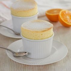 two dessert cups with powdered sugar on top and oranges in the back ground