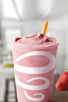 a pink smoothie in a cup with a straw next to it and a strawberry on the side