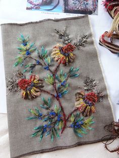 an embroidered piece of cloth with flowers and leaves on it, next to other items