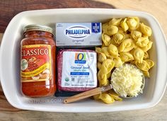 pasta, cheese and other ingredients in a white dish on a wooden table with a spoon