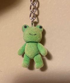 a green frog keychain hanging from a silver chain on a white wall background