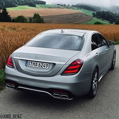 the rear end of a silver mercedes s - class coupe driving down a country road