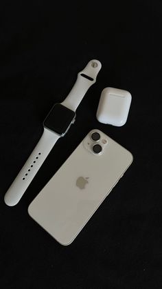 an apple watch sits next to its case and earbuds on a black background