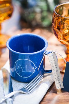 a blue cup sitting on top of a wooden table next to a fork and knife