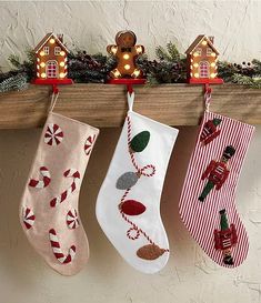 three christmas stockings hanging from a mantel with gingerbread houses and candy canes