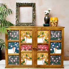 a wooden cabinet decorated with colorful tiles and potted plants next to a mirror on the wall