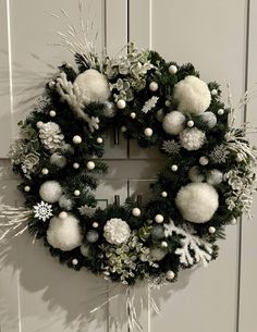 a christmas wreath hanging on a door with white balls and snowflakes around it