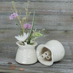 a white vase with flowers in it sitting on a wooden table next to some coins