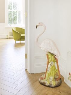 a flamingo statue sitting on top of a wooden floor next to a green chair