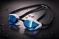 two goggles with blue and white lenses on top of raindrop covered water droplets