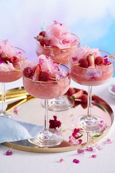 three glasses filled with ice cream and strawberries on a tray next to some flowers