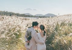 a bride and groom kissing in the middle of a field with tall grass on either side