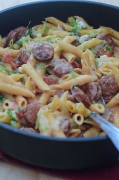 a skillet filled with pasta and sausages on top of a wooden table next to a fork