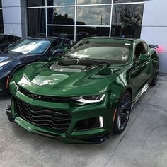 the green chevrolet camaro is parked in front of a building with several other cars