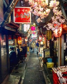 an alley way with people walking down it and signs hanging from the side of buildings