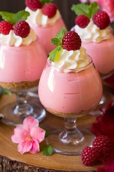 three desserts with raspberries and whipped cream in small glasses on a table