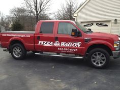 a red pickup truck parked in front of a garage with pizza wagon on the side