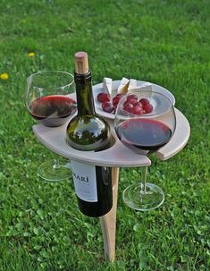 a wine bottle and two glasses sitting on a table in the grass with some fruit