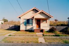 a small house sitting on the side of a road next to a fence and grass