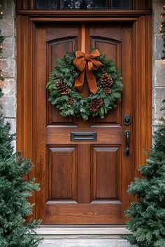 a christmas wreath on the front door of a house with evergreens and pine cones