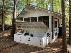 a small white building in the middle of some trees and dirt with lots of windows