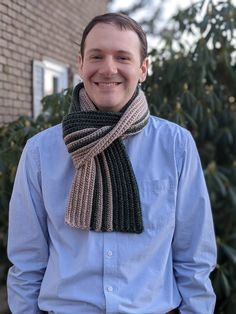 a man wearing a knitted scarf standing in front of a house smiling at the camera