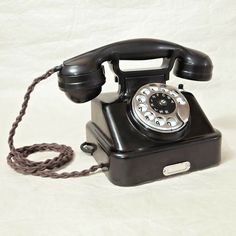 an old - fashioned black phone is sitting on a white sheet and has a cord attached to it