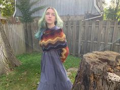 a woman with green hair standing in front of a tree stump and wearing a dress