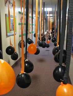 orange and black balloons are hanging from the ceiling in an office hallway that is decorated with art