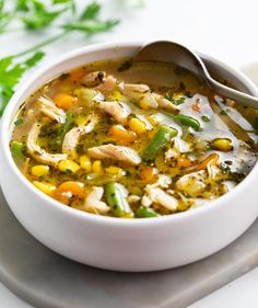 a bowl of chicken and vegetable soup on a white plate with a spoon next to it