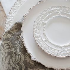 two white plates sitting next to each other on top of a cloth covered tablecloth