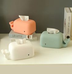 two elephant shaped tissue dispensers sitting on top of a white counter next to books