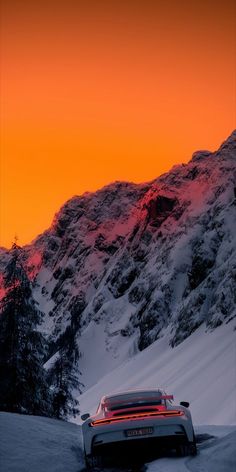 a car driving down a snow covered road in front of a mountain range at sunset