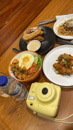 a wooden table topped with plates and bowls of food next to a yellow instant camera