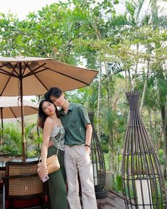 a man and woman standing next to each other in front of an umbrella on a patio