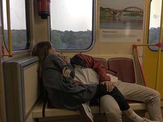 two people are sleeping on a train seat next to each other and looking out the window