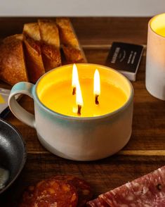 two candles sitting in a bowl next to some meat and bread on a cutting board