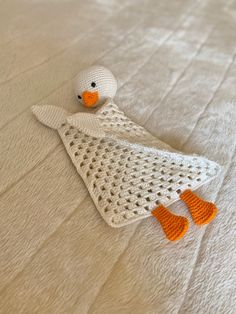 a crocheted white duck laying on top of a bed next to orange feet