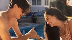 a man and woman sitting next to each other near a swimming pool with balloons in the air