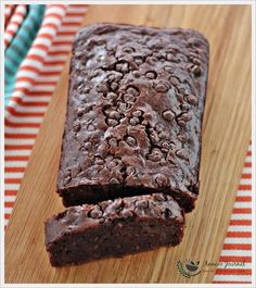 a loaf of chocolate cake sitting on top of a wooden cutting board next to a striped napkin