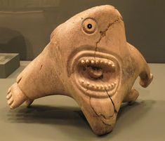 a clay sculpture of a fish with its mouth open and eyes wide open, sitting on a table