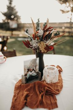 an arrangement of flowers in a vase sitting on top of a white table cloth covered table