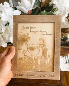 a person holding up a framed photo with flowers in the background and an inscription on it